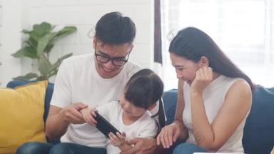 快乐的亚洲家庭爸爸，妈妈和女儿在网上玩着好玩的游戏，坐在家里的沙发上。自我隔离、待在家里、与他人保持距离、检疫以预防结肠炎.